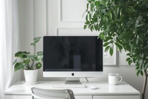 Minimalistiskt skrivbord med dator, tangentbord, växt och kaffemugg